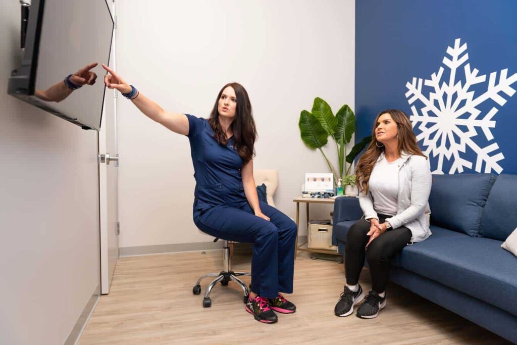 Sculptology provider reviewing CoolSculpting consult and treatment plan with patient in Lafayette treatment center with a large monitor and a blue sitting area. 