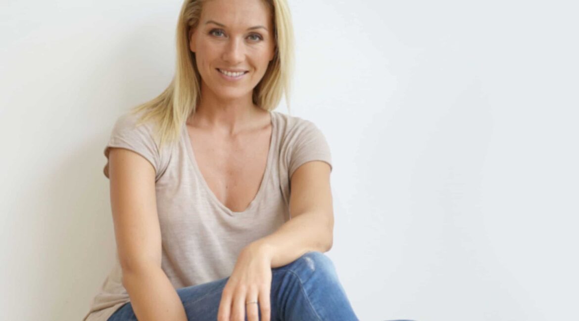 Beautiful blond woman sitting on floor against white wall