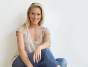 Beautiful blond woman sitting on floor against white wall