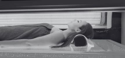 Patient lying on a medical imaging table with head supported in a curved cushion inside a large hospital scanner.