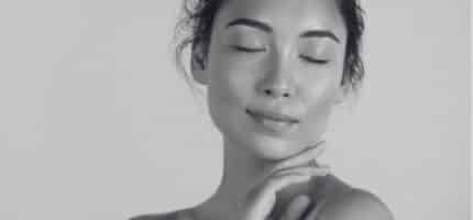 Close-up of a calm woman with eyes closed, gently touching her neck.